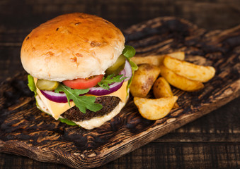 Fresh organic beef burger with cheese  and sauce with vegetables and potato vedges on wooden chopping board.