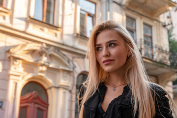 Fototapeta na wymiar Waist up portrait of attractive stylish blonde woman with loose hair walks among old city center
