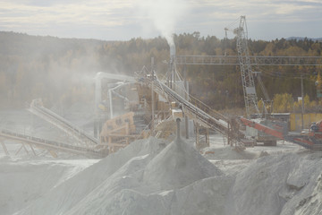 Silhouette in a cloud of dust of equipment for crushing rock and sorting into fractions at a mining...