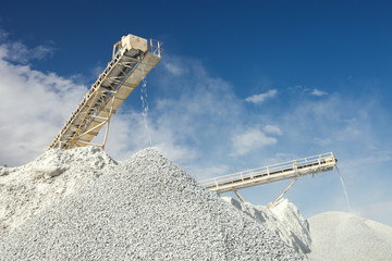 Conveyor belt at the equipment for crushing and sorting rocks into fractions at a mining enterprise on the background of the blue sky with clouds.