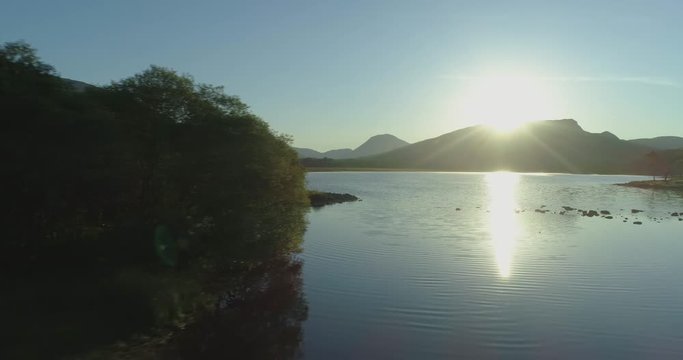 Low travelling aerial passing forest on the edge of Loch Awe to reveal the ancient Kilchurn Castle in the Western Scottish Highlands