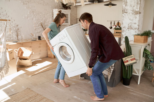 Side view of barefoot content man and woman carrying white washing machine while moving to new house
