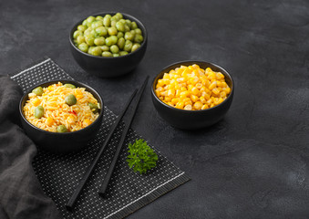 Black bowl with boiled organic basmati vegetable rice with black chopsticks on placemat with linen towel. Yellow corn and green peas with paprika slices.