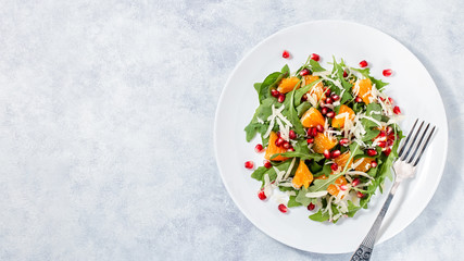Fresh green organic salad with raw ingredients close up. Tasty salad with arugula, orange slices, pomegranate and cheese on white plate, top view. Healthy eating, dieting concept