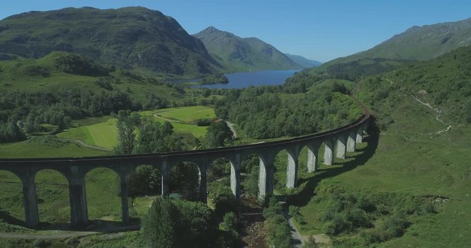 Aerial approaching of Glen Finnan Viaduct in the Scottish Highlands with Loch Shiel in the background on a sunny day