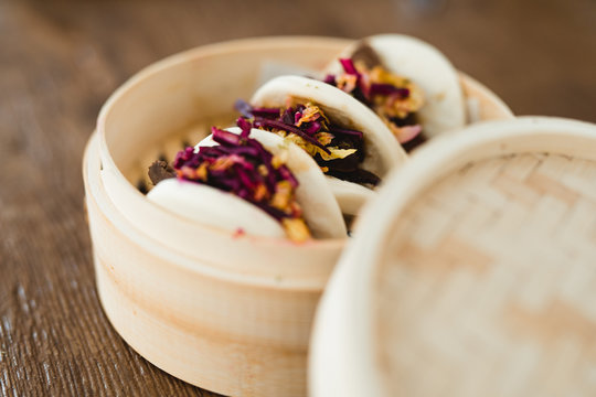 Closeup of traditional Asian sandwich steamed bun with meat and vegetables in bamboo steamer placed in wooden table