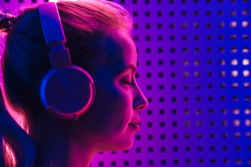 Image of woman listening to music with headphones over neon illumination