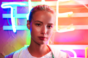 Image closeup of young woman standing over multicolored neon text sign