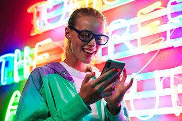 Image of woman in 3D glasses holding smartphone over neon text sign