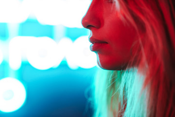 Image of young woman standing over multicolored neon text sign outdoors