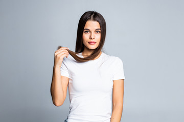 Portrait of smiling young beautiful woman holding ends of her long brown hair on white background