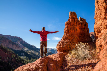 Hiker near red rock summit with arms out looking at the desert view.