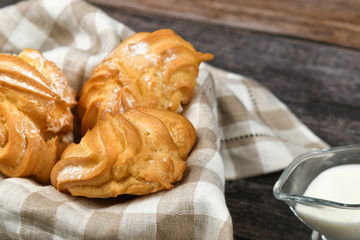 Choux cake with milk on a dark wooden background. In a basket on a checkered towel. View from above. Chic with cottage cheese. Small custard cakes in wicker bowl on wooden background