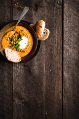 Carrot and red lentil cream soup with black sesame seeds, fresh parsley leaves and cream. Served  with bread in dark bowl. Dark wooden background, copy space.