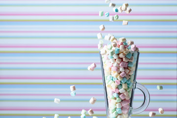 Marshmallows fall in mug. Small colorful marshmallows in glass mug on a striped background.