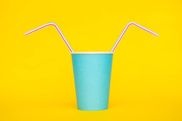 Blue paper cup with drinking colored plastic straws on yellow background. Set for party. Minimalist Style. Copy, empty space for text