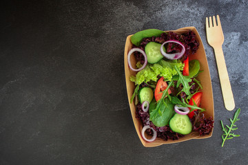 Healthy salad, leaves mix salad in paper disposable tableware (mix micro greens, cucumber, tomato, onion, other ingredients). food background. copy space