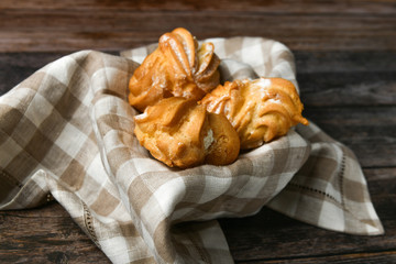 Choux cake on a wooden background. In a basket on a checkered towel. The apartment was lying. View from above. Chic with cottage cheese. Small custard cakes in wicker bowl on wooden background