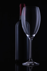 Red wine glass and a wine bottle with reflections on black background