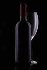 Red wine glass and a wine bottle with reflections on black background