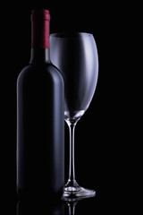 Red wine glass and a wine bottle with reflections on black background