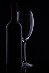 Red wine glass and a wine bottle with reflections on black background