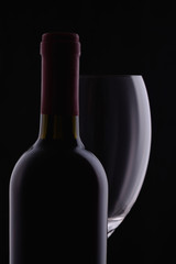Red wine glass and a wine bottle with reflections on black background