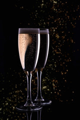 Two glasses with white wine champagne on a black background with golden bokeh. Festive concept.