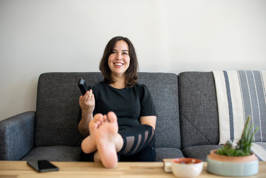 Woman sitting on couch with feet up holding remote