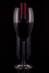 Elegant red wine glass and black wine bottle on black background