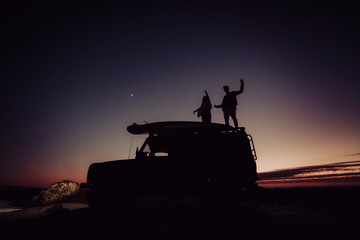 couple standing on top of a 4x4 while camping during the blue hour