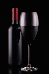 Elegant red wine glass and black wine bottle on black background