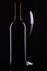 Elegant red wine glass and black wine bottle on black background
