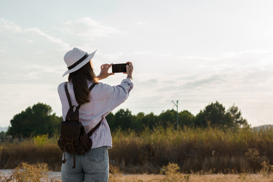 Young woman is taking a picture with her smartphone in a field. Adventure, technology