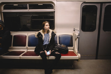 Young woman listening music on smart phone traveling in subway train