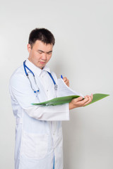 A doctor in a white coat with a stethoscope on his neck reads tests in a green folder. One on a white background.