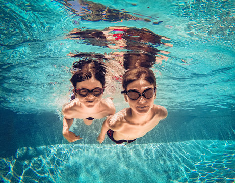 Underwater image of two boys swimming beside eachother in a pool.