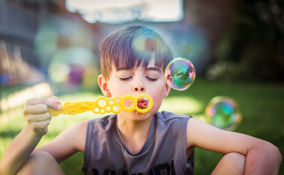 Young boy blowing bubbles outdoors on a summer day.