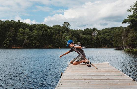 Boy Catching A Fish With A Fishing Rod On The End Of A Dock On A Lake.