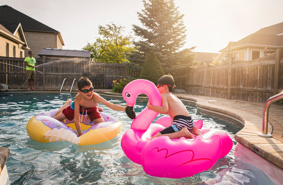 Two boys playing in a swimming pool on inflatable pool toys. - Powered by Adobe