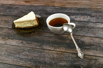Cheesecake with coffee on a dark wooden background. view from above. A cheesecake next to it on a brown wooden background. retro cup. Coffee in a coffee shop, copy space.