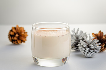 Traditional Christmas cocktail Eggnog with eggs, alcohol, grated nutmeg and cinnamon closeup. Sweet traditional drink on wooden table with red decorations and pine cones