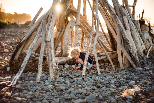 Small child playing in driftwood structure at dusk