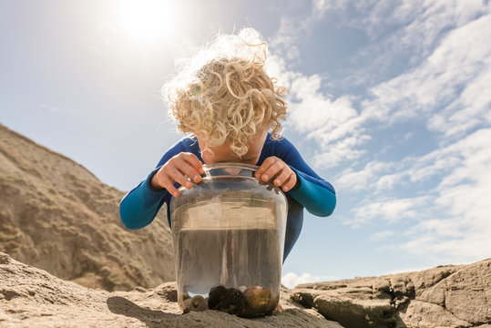 Curly haired child looking in bucket at a beach on a sunny day