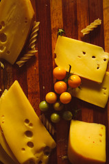 Sliced cheese on wooden desk with cut vegetables and knife