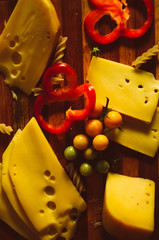 Sliced cheese on wooden desk with cut vegetables and knife