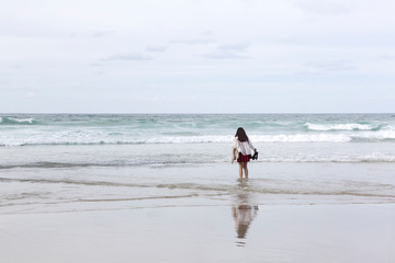 Chica joven vestida con falda y chaqueta mojándose los pies en el mar en un día nublado