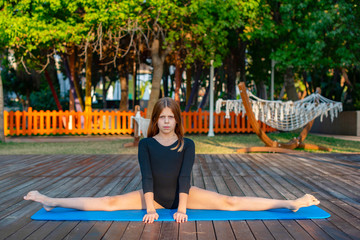 girl in black gymnastic leotard practicing on the street, the concept of yoga and a healthy...