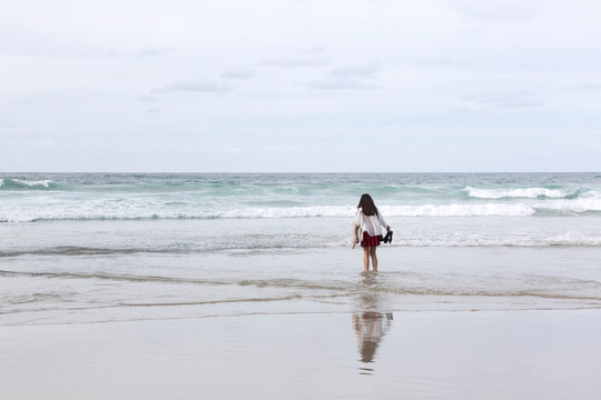 Chica joven vestida con falda y chaqueta moj&aacute;ndose los pies en el mar en un d&iacute;a nublado