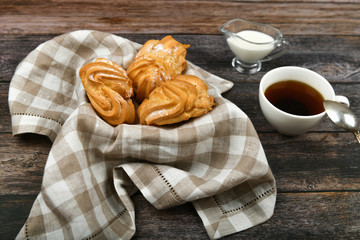 Choux cake with coffee on a wooden background. In a basket on a checkered towel. View from above. Chic with cottage cheese. Small custard cakes in wicker bowl on wooden background
